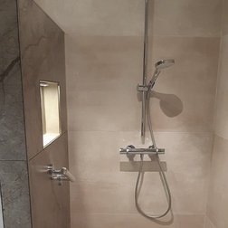 Der Duschbereich zeigt glatte, beige Fliesen und eine stilvolle Wandnische, die für Pflegeprodukte genutzt werden kann.