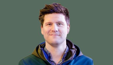 Ein Mann mit kurzem, vollem Haar lächelt freundlich in die Kamera, während er einen farbenfrohen Hemdkragen trägt.