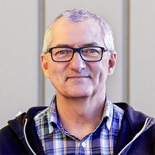 Ein freundliches Porträt eines älteren Mannes mit Brille Ein älterer Mann mit Brille und grauen Haaren lächelt freundlich in die Kamera, während er einen karierten Hemd trägt.