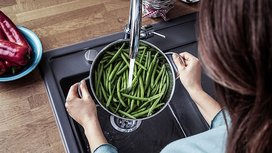 Eine Frau haelt ein Topf mit Bohnen unter der laufenden Kuechenspuehle