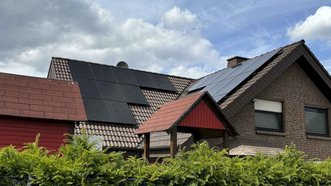 Zwei benachbarte Häuser, eines mit Solarpanels, umgeben von üppigem Grün und einem dramatischen, bewölkten Himmel.