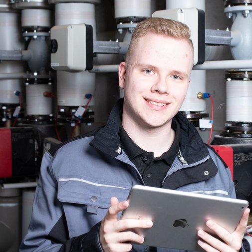 Ein junger Anlagenmechaniker vor einer Heizungsanlage, der ein Tablet hält 